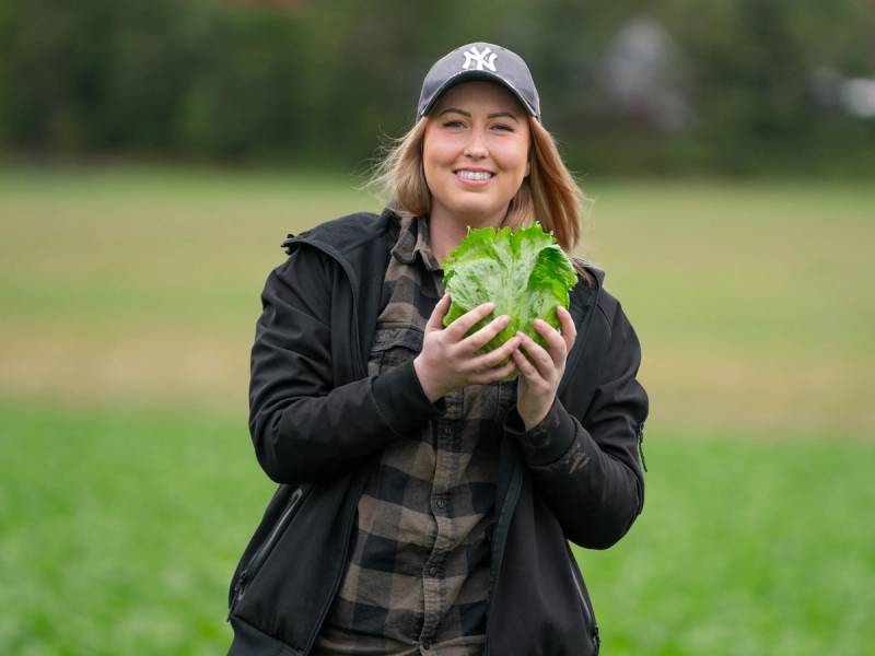 En person holder en stor grønn salat i hendene ute i en park, med trær og gress i bakgrunnen.