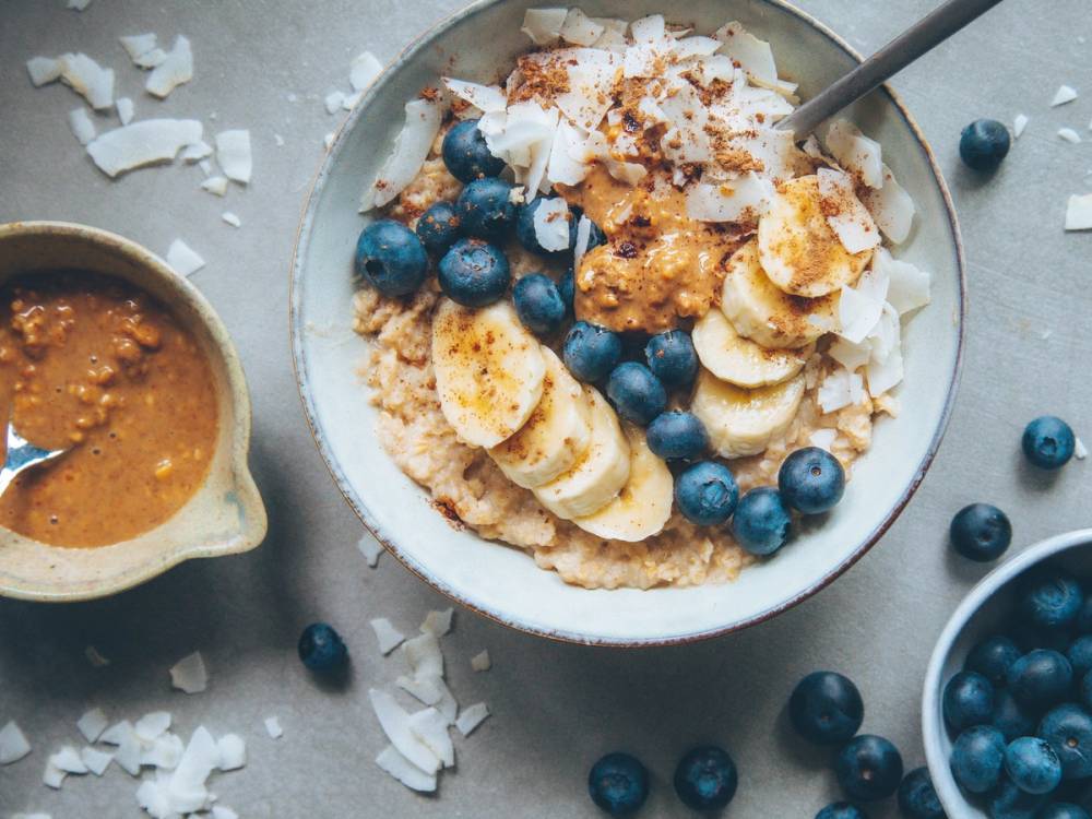 Havregrøt med bananskiver og blåbær toppet med kokosflak, ser ut til å være en sunn frokostrett.