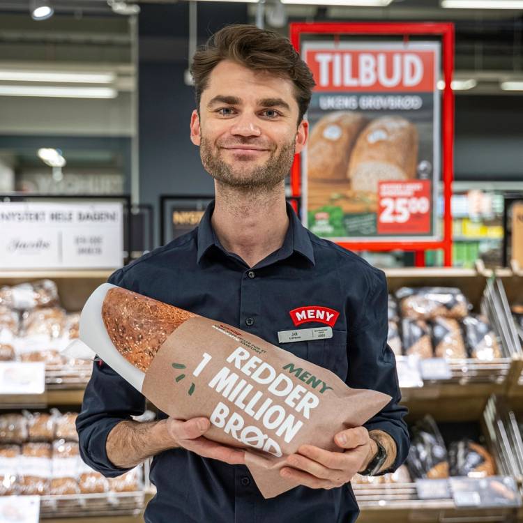 En ansatt i Meny-butikk holder et brød med reklame for Røder og millioner av brød, foran en reklameskilt med tilbud på brød.