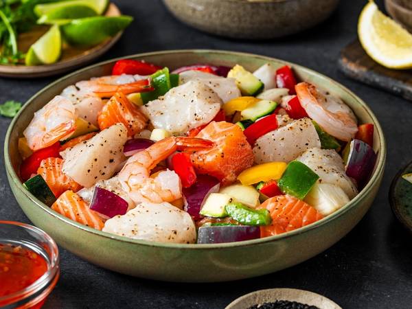 En bolle med en salat bestående av scampi, agurk, paprika og rødløk, omgitt av små skåler med lime, krydder og saus.
