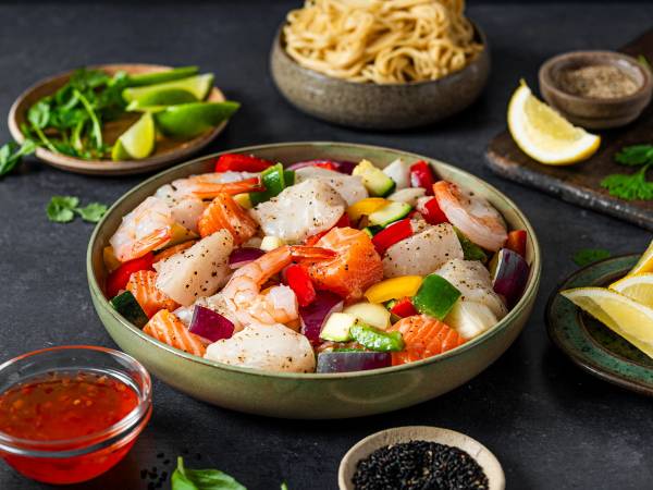 En bolle med en salat bestående av scampi, agurk, paprika og rødløk, omgitt av små skåler med lime, krydder og saus.