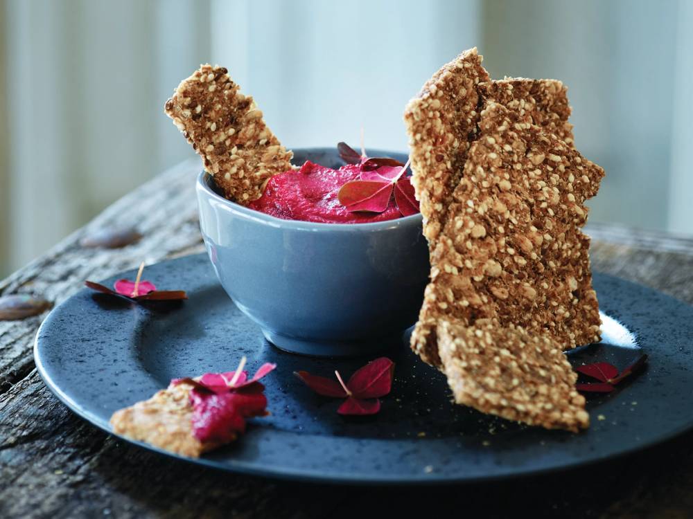 En skål med rosa is omgitt av sprø kjeks og rosa blomster på en svart tallerken.