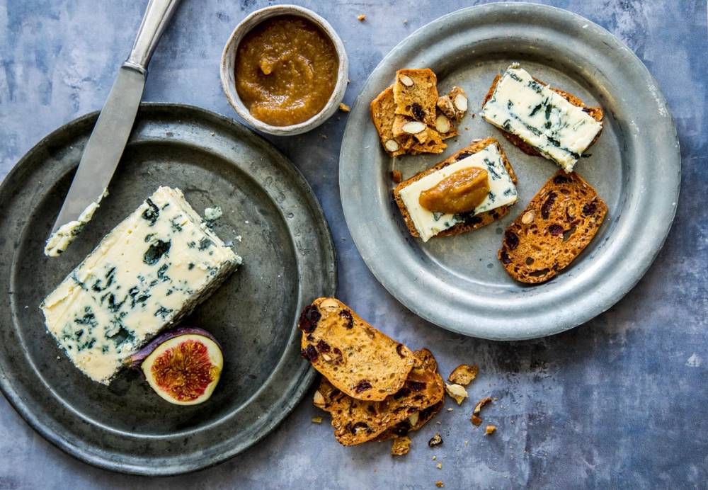 Blåmuggost servert med kjeks og tørket frukt på to tallerkener.
