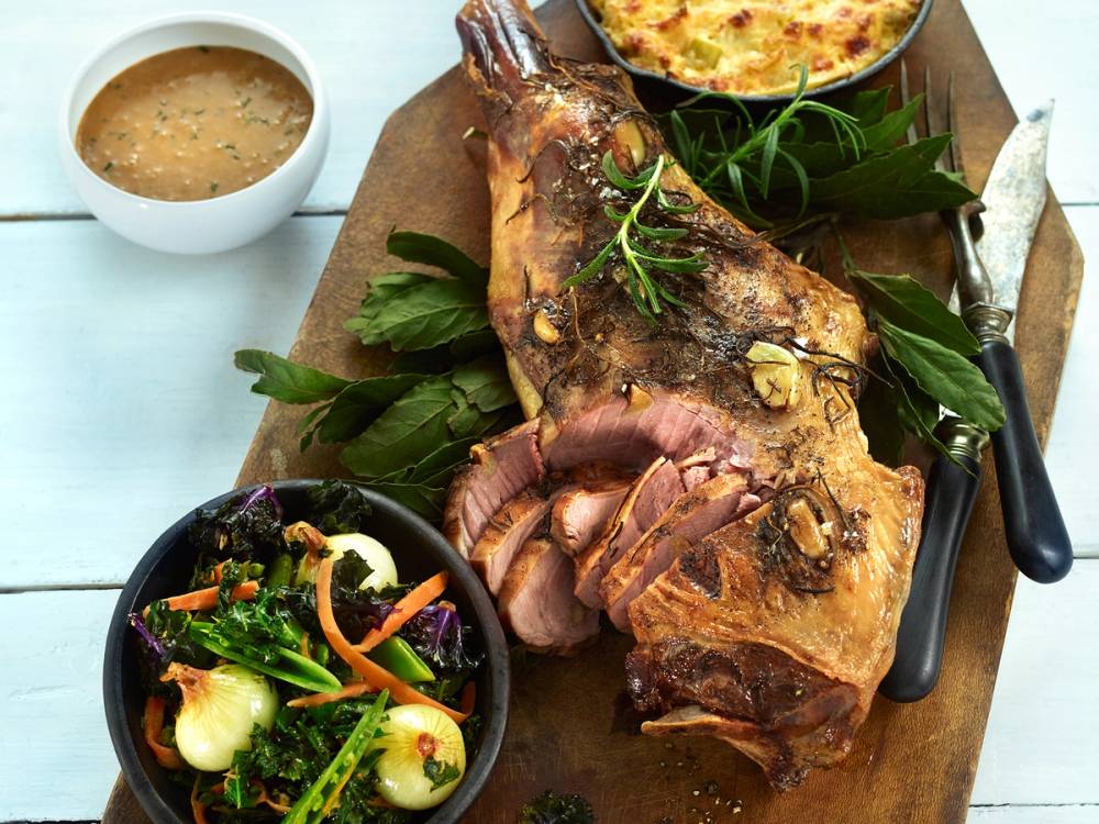 Langtidsstekt lammestek med grønnsaker og saus på et serveringsfat, med en salat ved siden av.