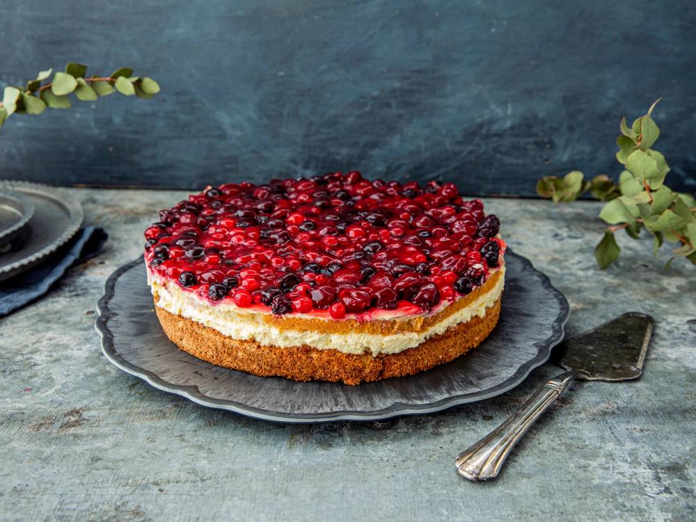 En vaniljekake med bær på toppen på en svart tallerken, plassert på et bord med en skje ved siden av.