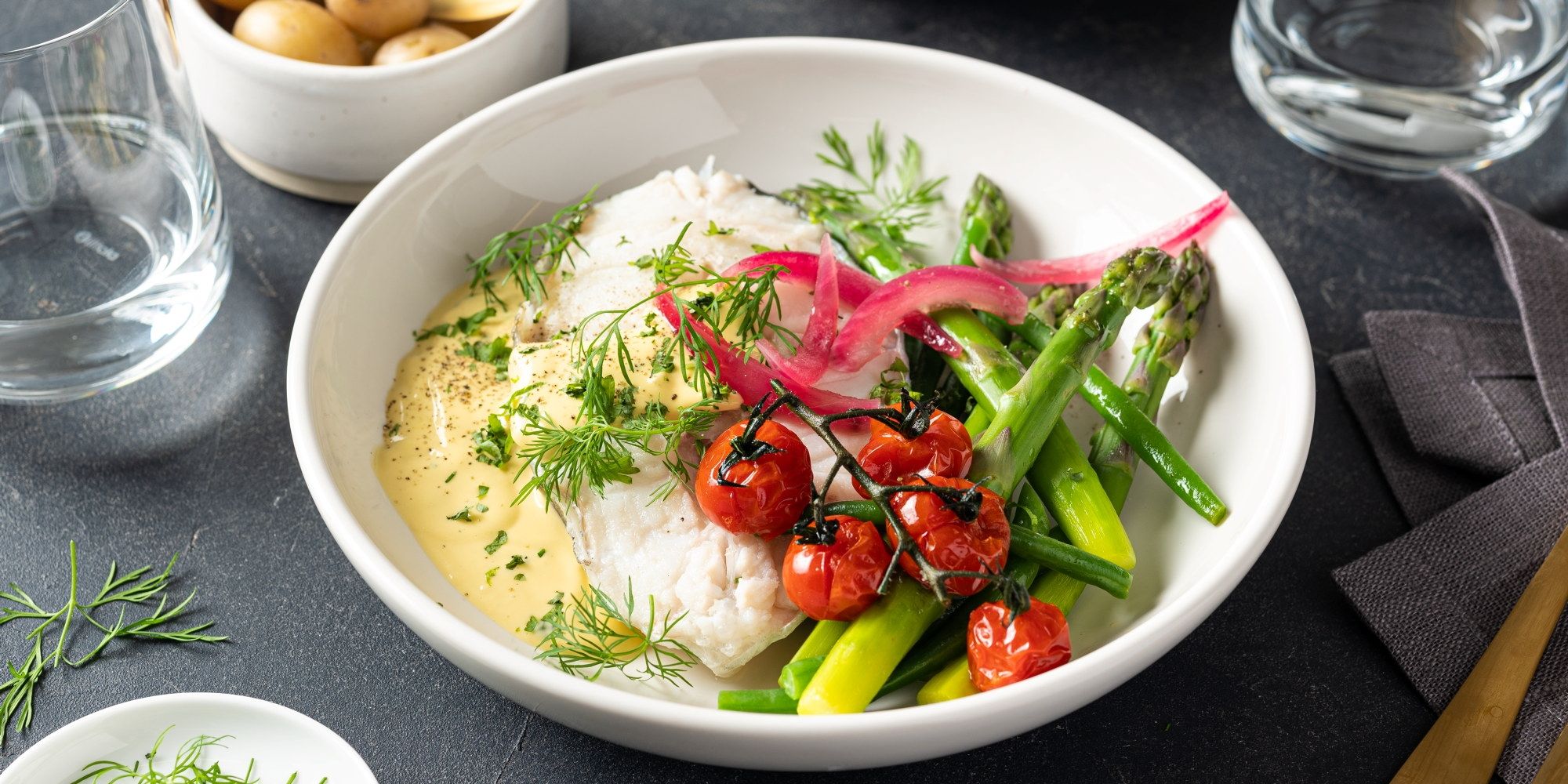 Skrei med hollandaise saus servert med grønnsaker og urter på en hvit tallerken