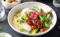 Skrei med hollandaise saus servert med grønnsaker og urter på en hvit tallerken