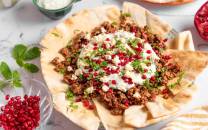 Liba brød med lamme kjøttdeig, toppet med yoghurt, granateple og frisk mynte, på et hvitt bord.