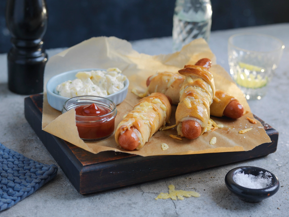 Innbakte pølser med revet ost på et serveringsfat med tilbehør som ketchup og rømme.