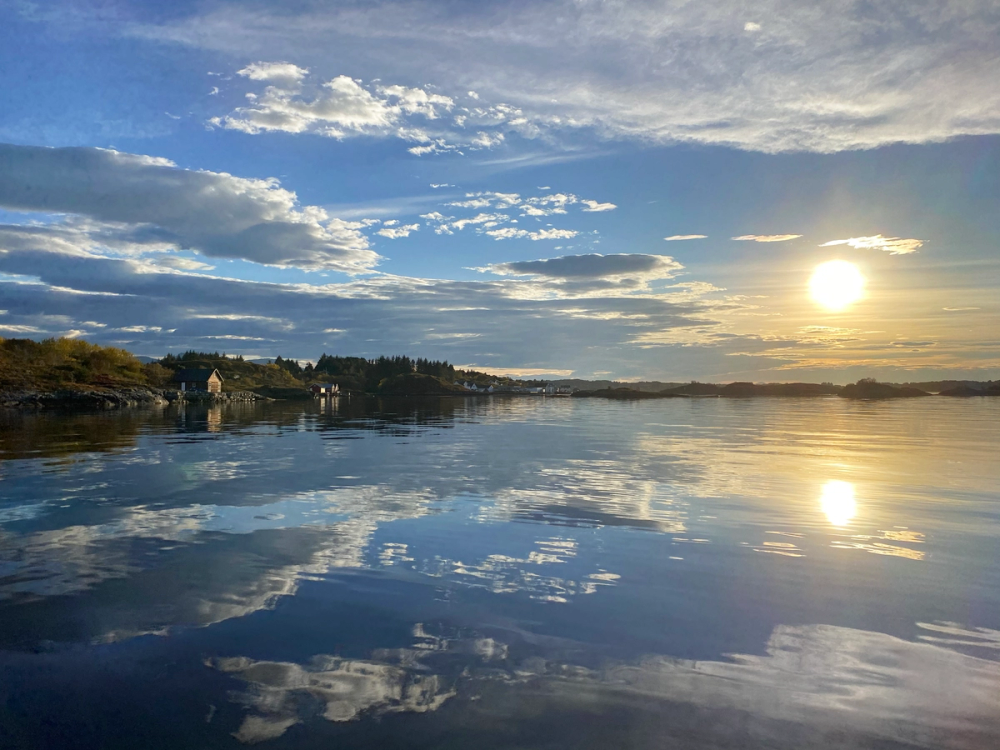 Utsikt over Juvika med vann og speilende himmel under solnedgang eller soloppgang.