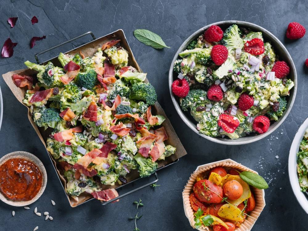 To salatboller med grønnsaker og bær, og en salat i en stor bolle med friske bær og grønnsaker, på en mørk overflate.