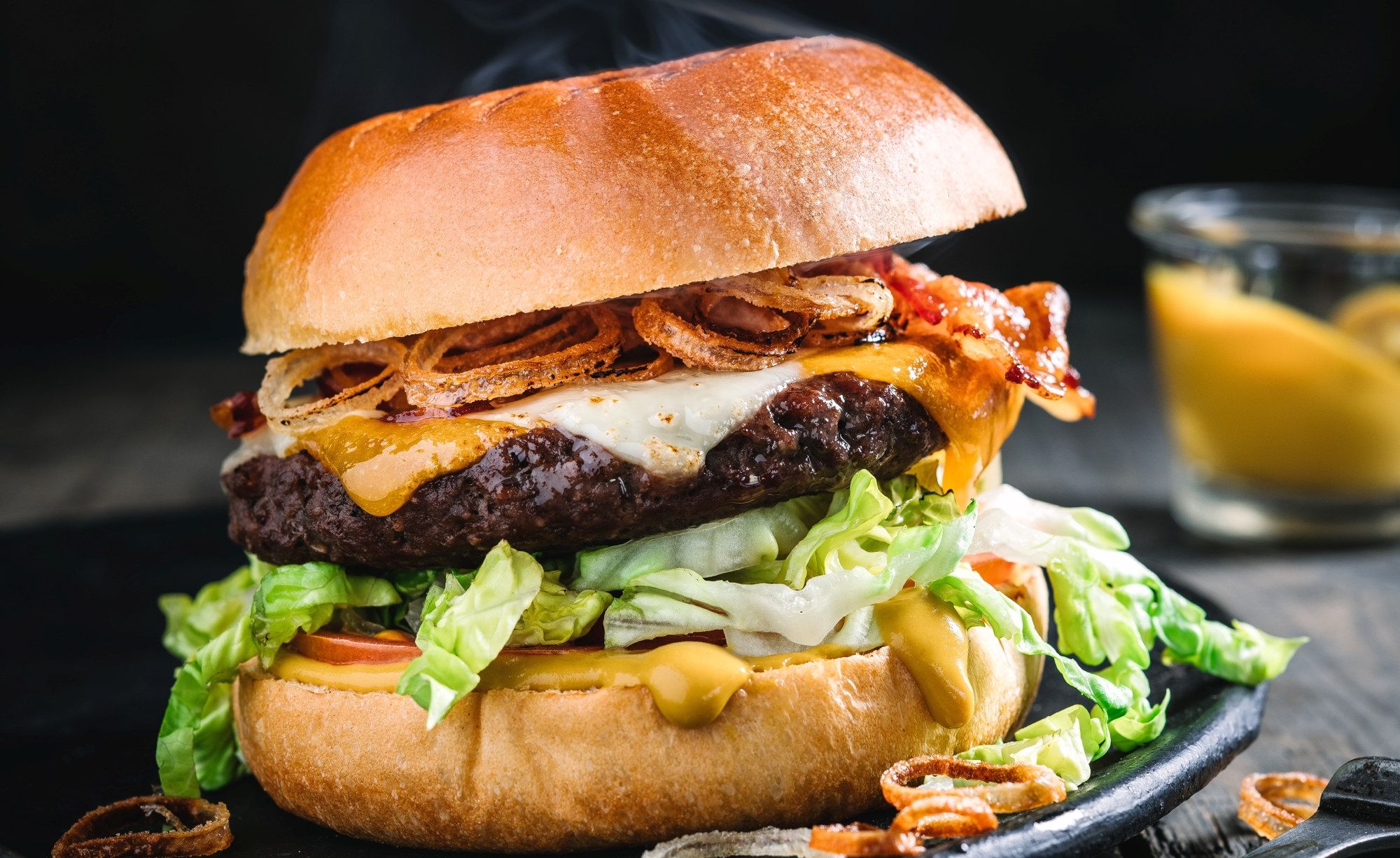 En saftig hamburger med kjøttkake, ost, bacon, salat og dressing i et hamburgerbrød.