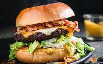 En saftig hamburger med kjøttkake, ost, bacon, salat og dressing i et hamburgerbrød.