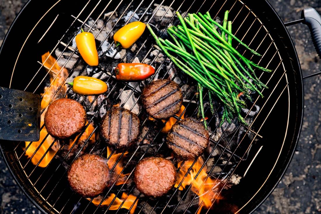 Vegetariske burgerboller og grønne asparges grilles på en grill med glødende kull.