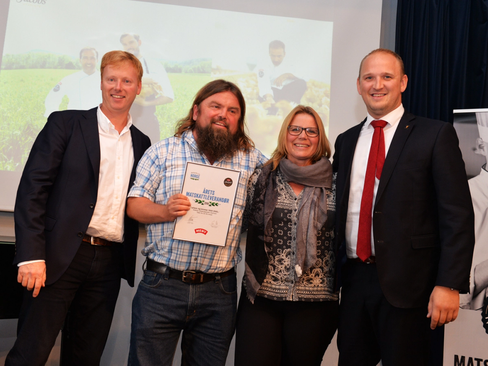 En gruppe mennesker står sammen under en seremoni, hvor en person holder et diplom, og det er en skjerm i bakgrunnen med teksten 'Matskattstipend 2016'.