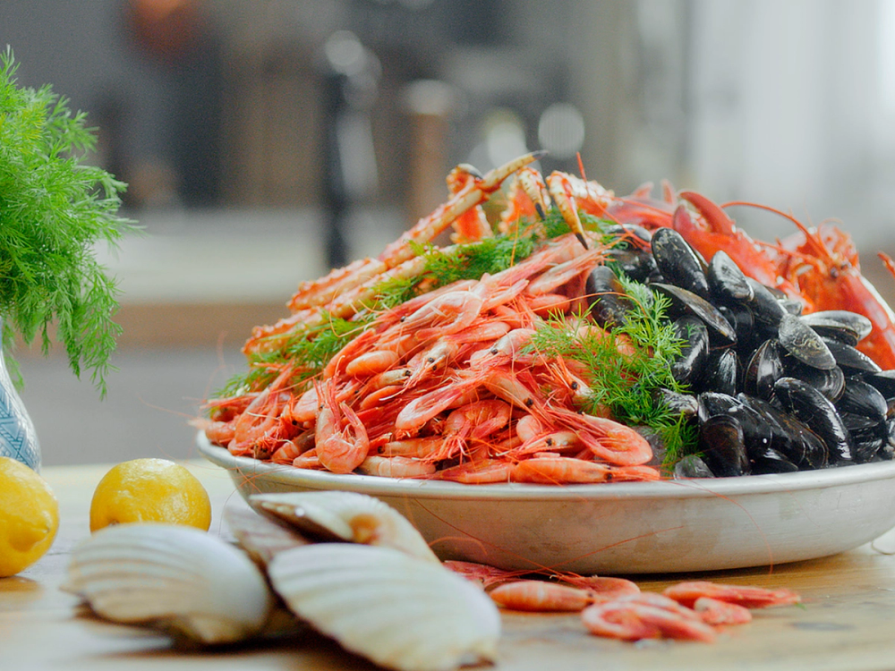 En tallerken med skalldyr som reker, blåskjell og krabbe, omgitt av sitroner og hvitløk, på et kjøkkenbord.