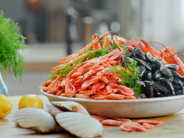 En tallerken med skalldyr som reker, blåskjell og krabbe, omgitt av sitroner og hvitløk, på et kjøkkenbord.