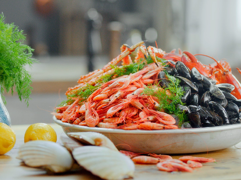 En tallerken med skalldyr som reker, blåskjell og krabbe, omgitt av sitroner og hvitløk, på et kjøkkenbord.