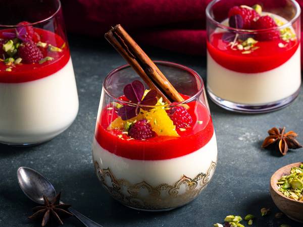 Panna cotta med jordbærsaus, frukt og krydder på toppen, servert i små glass.