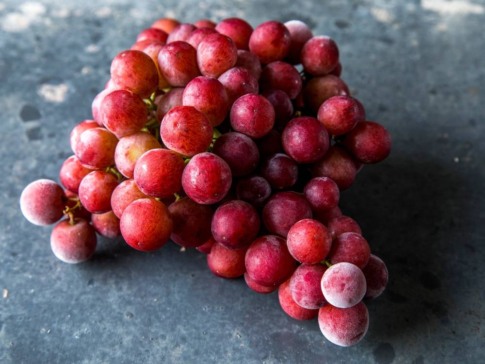 En klase med frosne røde druer liggende på en mørk overflate.