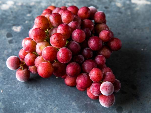 En klase med frosne røde druer liggende på en mørk overflate.
