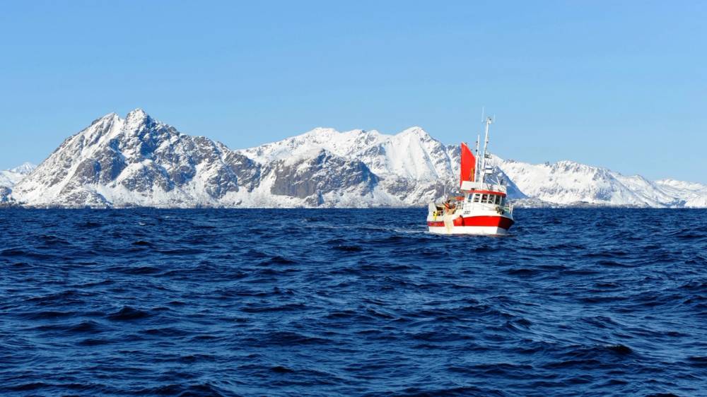Fiskebåt på åpent hav, foran snødekte fjell.