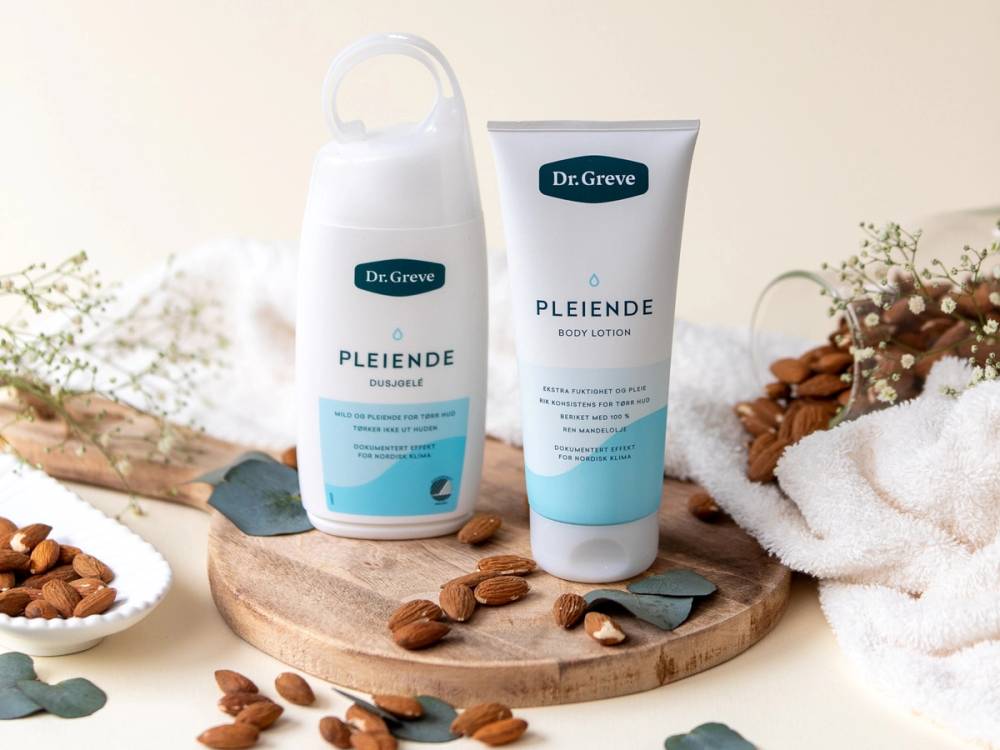 To pleiende hudpleieprodukter fra Dr. Greve plassert på en rund treplate med nøtter og tørkede blomster rundt, på et lyst bakgrunn.