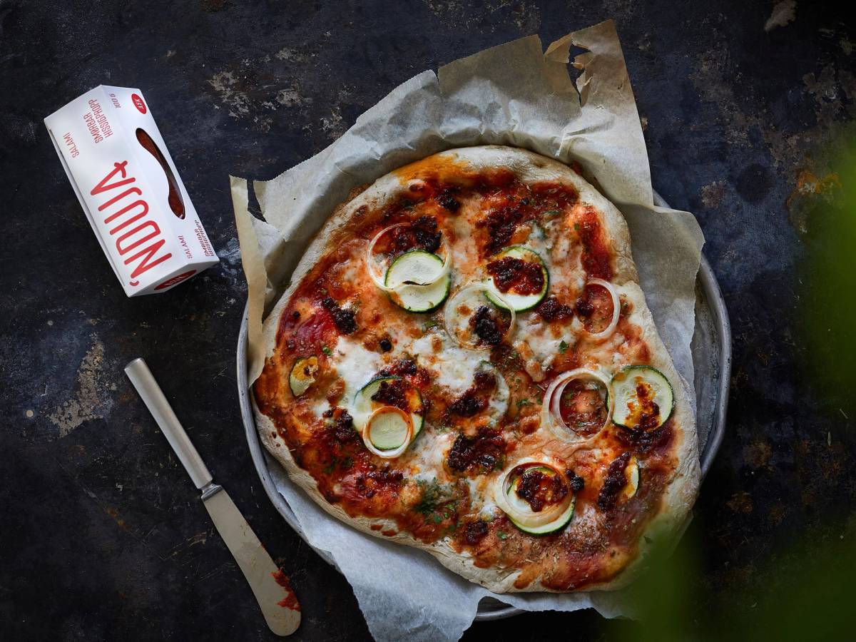 En pizza med nduja, ost og skiver av jalapeño på et stykke papir, med en liten melkekartong og en trepinne ved siden av.