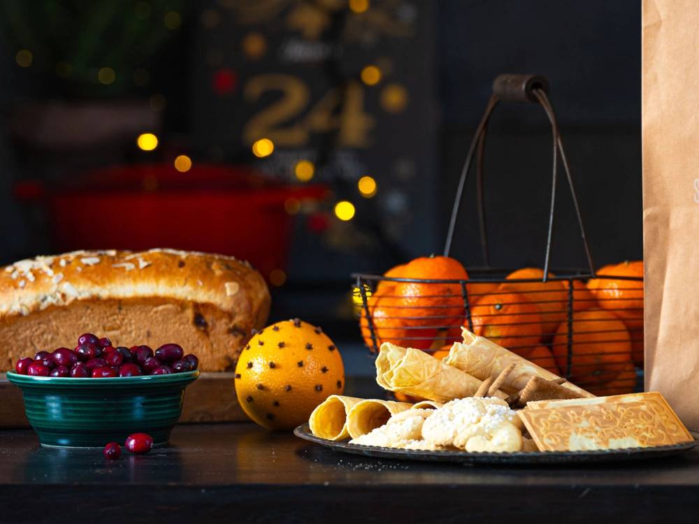 Julebilde med en kalender, klementiner, en kake, og julekuler på et bord med julelys i bakgrunnen.