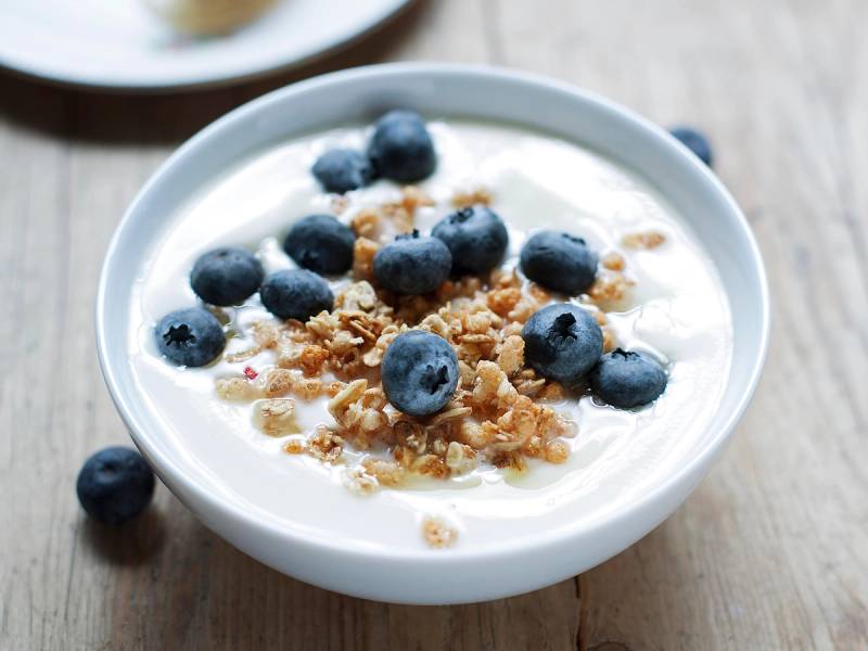 En skål med yoghurt toppet med blåbær og crunchy granola, plassert på et trebord