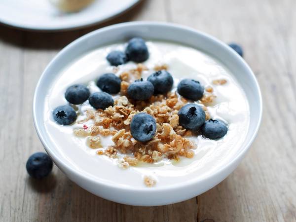 En skål med yoghurt toppet med blåbær og crunchy granola, plassert på et trebord