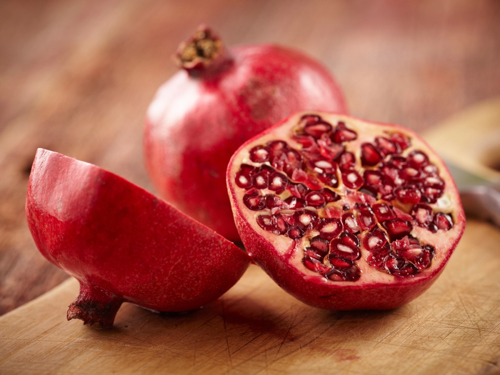 Et halvt granateple med frø og en hel granateple på et treverk, klar til å spises.