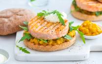 Lakseburger med mango, toppet med en klatt rømme og frisk grønn urter, servert på en flat brødskive med en side av mango- og sitrusdressing.