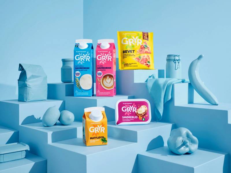 Ulike Gryr-produkter og en banan er plassert på hvite plattformer mot en blå bakgrunn.