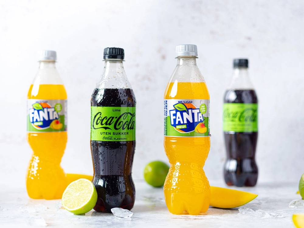 To flasker med Fanta og Coca-Cola, samt en lime og en sitron på et hvitt bord, med en lys bakgrunn.