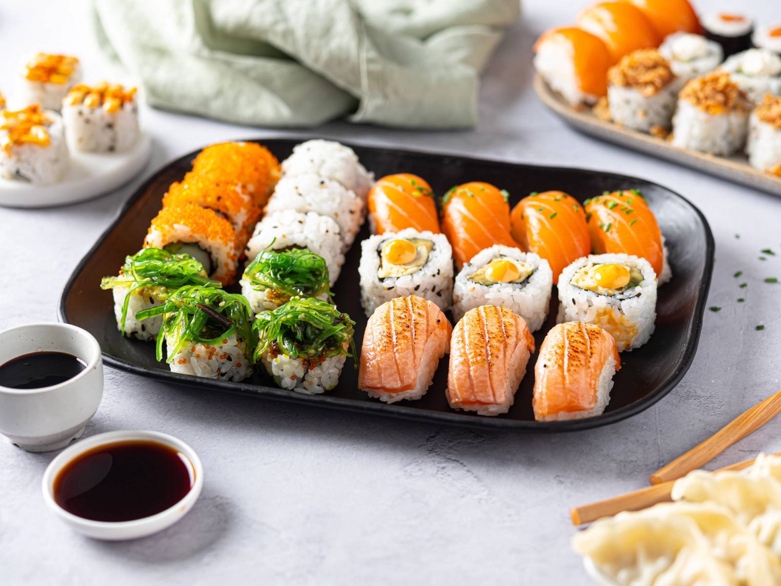 Ulike typer sushi på en svart serveringsfat med soyasaus og ingefær ved siden av.