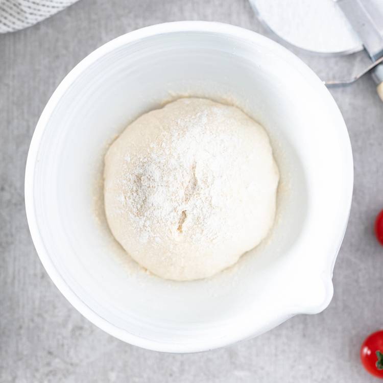 Pizzadeig formet til en kvadrat i en hvit bolle på en grå overflate.