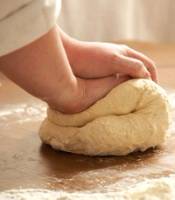 En person som knar deigen med hånden på et bord, med mel rundt omkring.