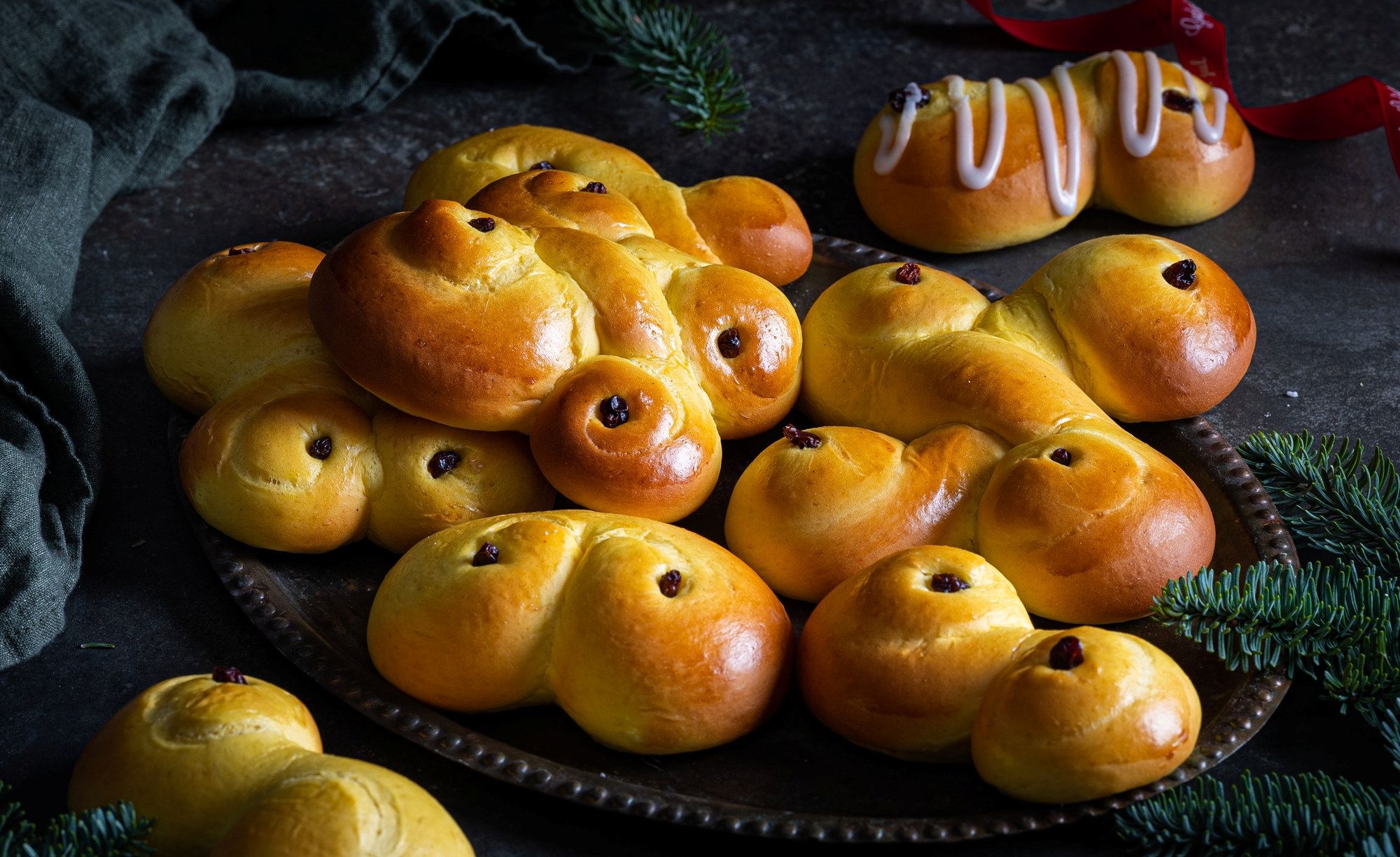 Lussekatter og julekaker på et fat med grønne grener rundt, klar til jul.