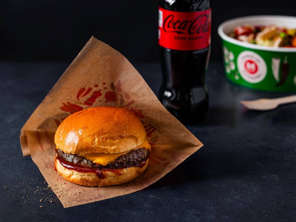 Hamburger med kjøttkake, Coca-Cola-flaske og en skål med mat på en svart bakgrunn