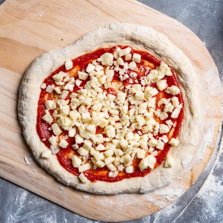 Pizza med tomatsaus og revet ost på en rund deig, klar for steking, plassert på en treplate.