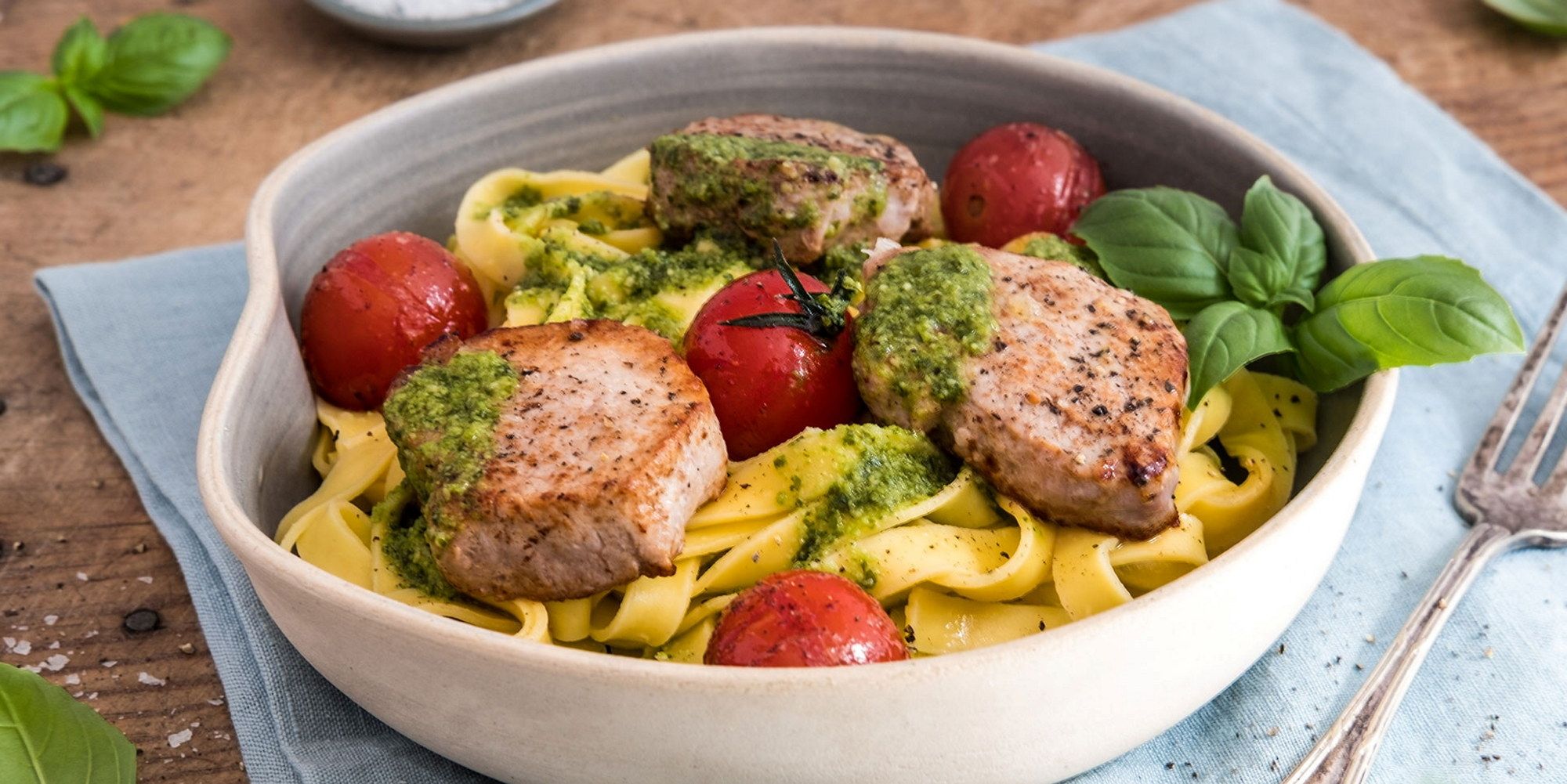 Pasta med svinefilet, cherrytomater og pesto i en hvit skål, ser ut til å være et måltid med pasta og kjøtt.