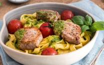 Pasta med svinefilet, cherrytomater og pesto i en hvit skål, ser ut til å være et måltid med pasta og kjøtt.