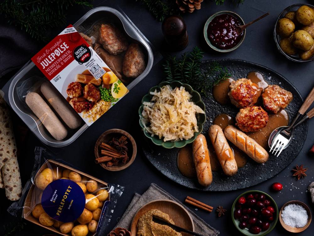 Julepølse med tilbehør som potetstappe, kjøttboller, og julegodt på et svart bord