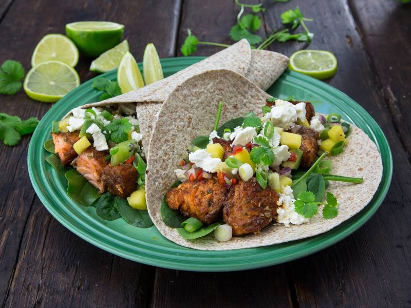 Fisketacos med grønnsaker, ost og lime på en grønn tallerken, omgitt av limebåter og urter.