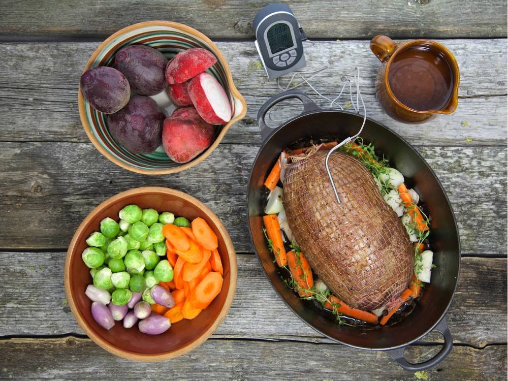 Elgstek på en tallerken omgitt av grønnsaker, frukt, en kopp med saus og en mobiltelefon på et trebord.