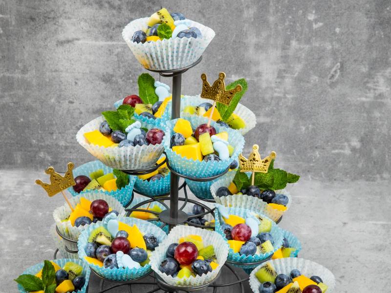 En treetasjes kakepynt med små kaker og frukt, dekorert med fargerike godteri og små kakefigurer, satt opp som en babyshower-dekorasjon.