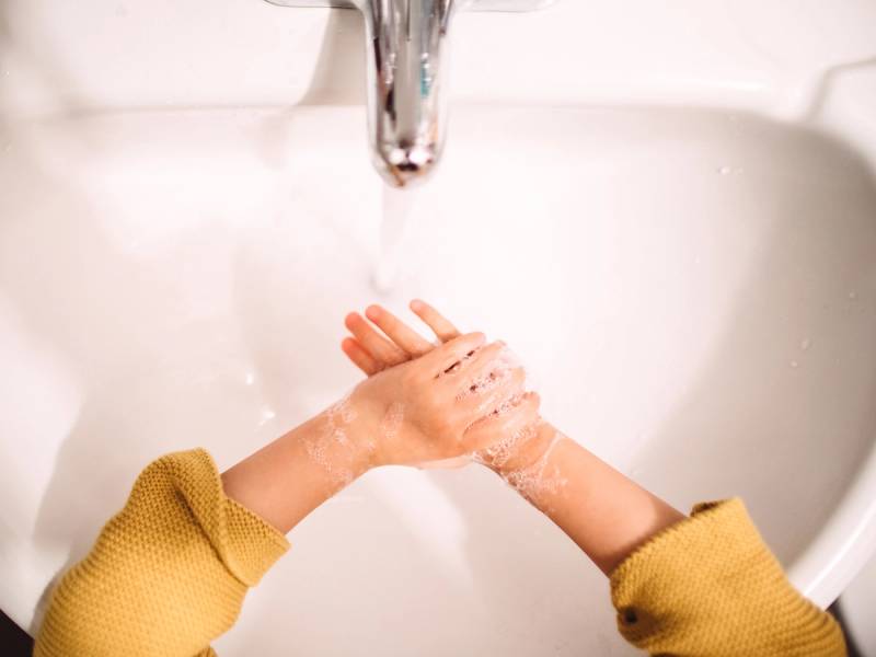 Barn som vasker hendene under en vannkran i et vaskeskap