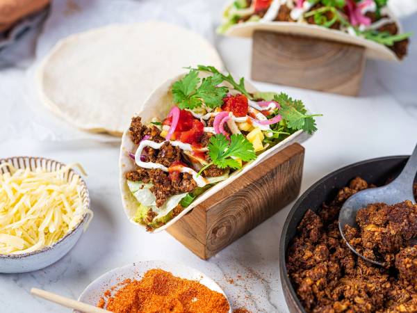 Vegetarisk taco med deig, grønnsaker og krydder, servert i en tacobestikkelse på en hvit bakgrunn.