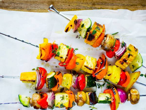 Fargerike spyd med grillet grønnsaker og kjøtt på en grillfest, plassert på et hvitt underlag.